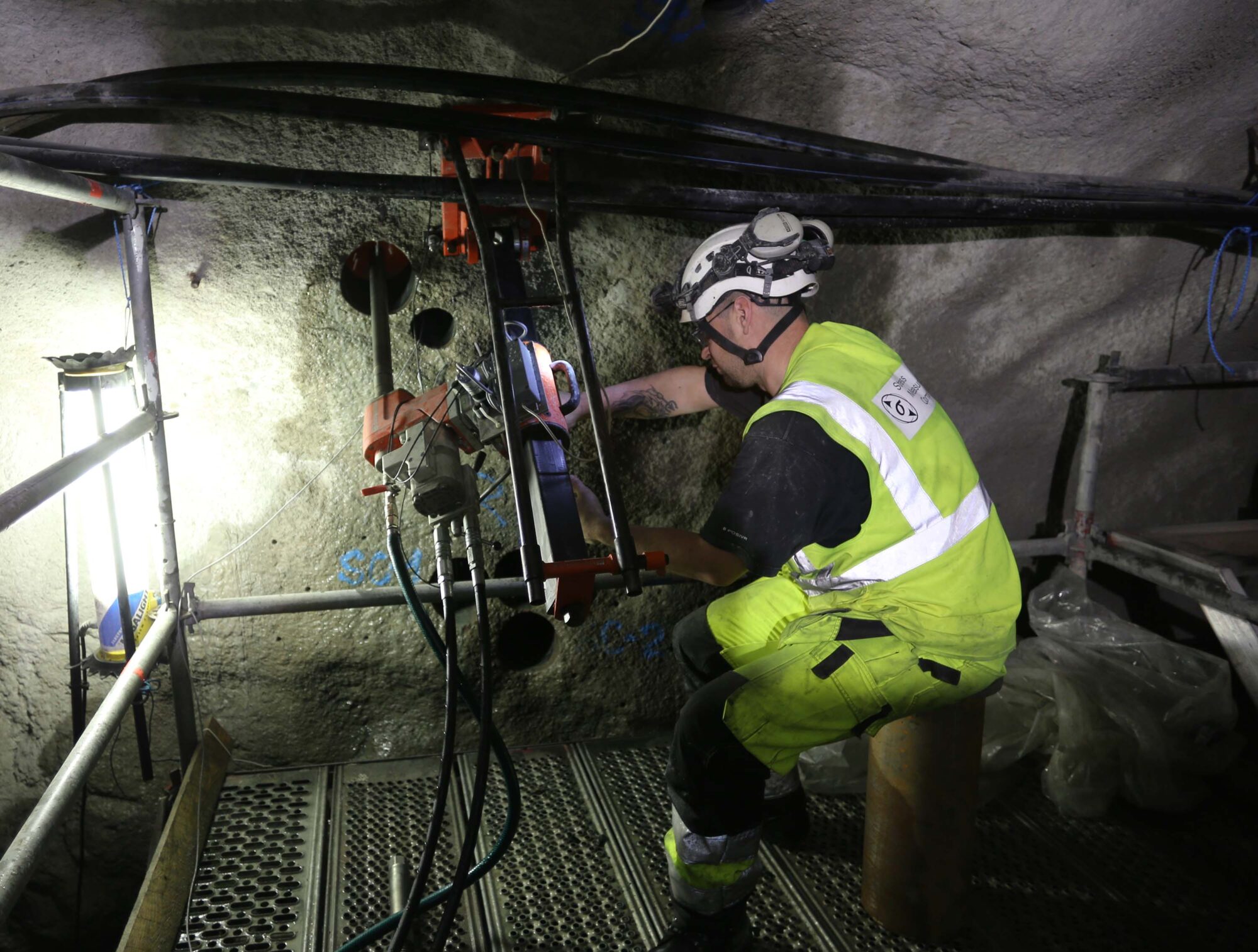 A man wearing yellow work clothes is drilling holes in a tunnel.
